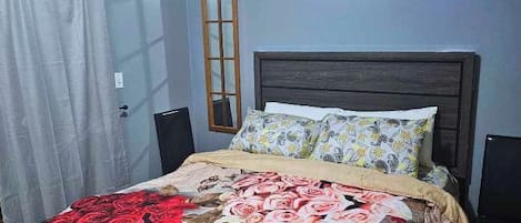 A bedroom with a bed, a window, a door, and a painting on the wall.