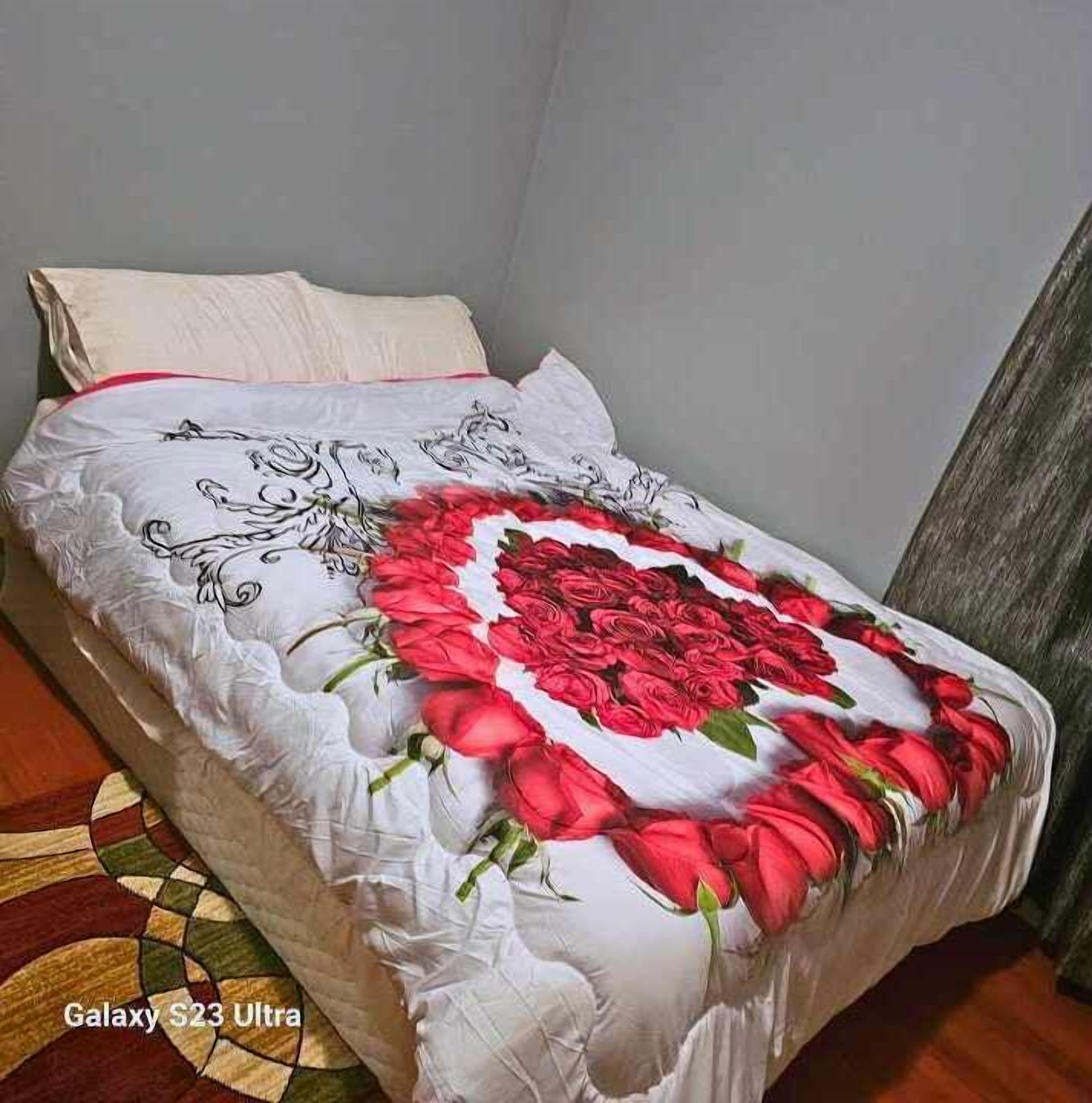 Un lit recouvert d’une courtepointe blanche ornée d’un grand motif représentant une rose rouge et de motifs floraux noirs.