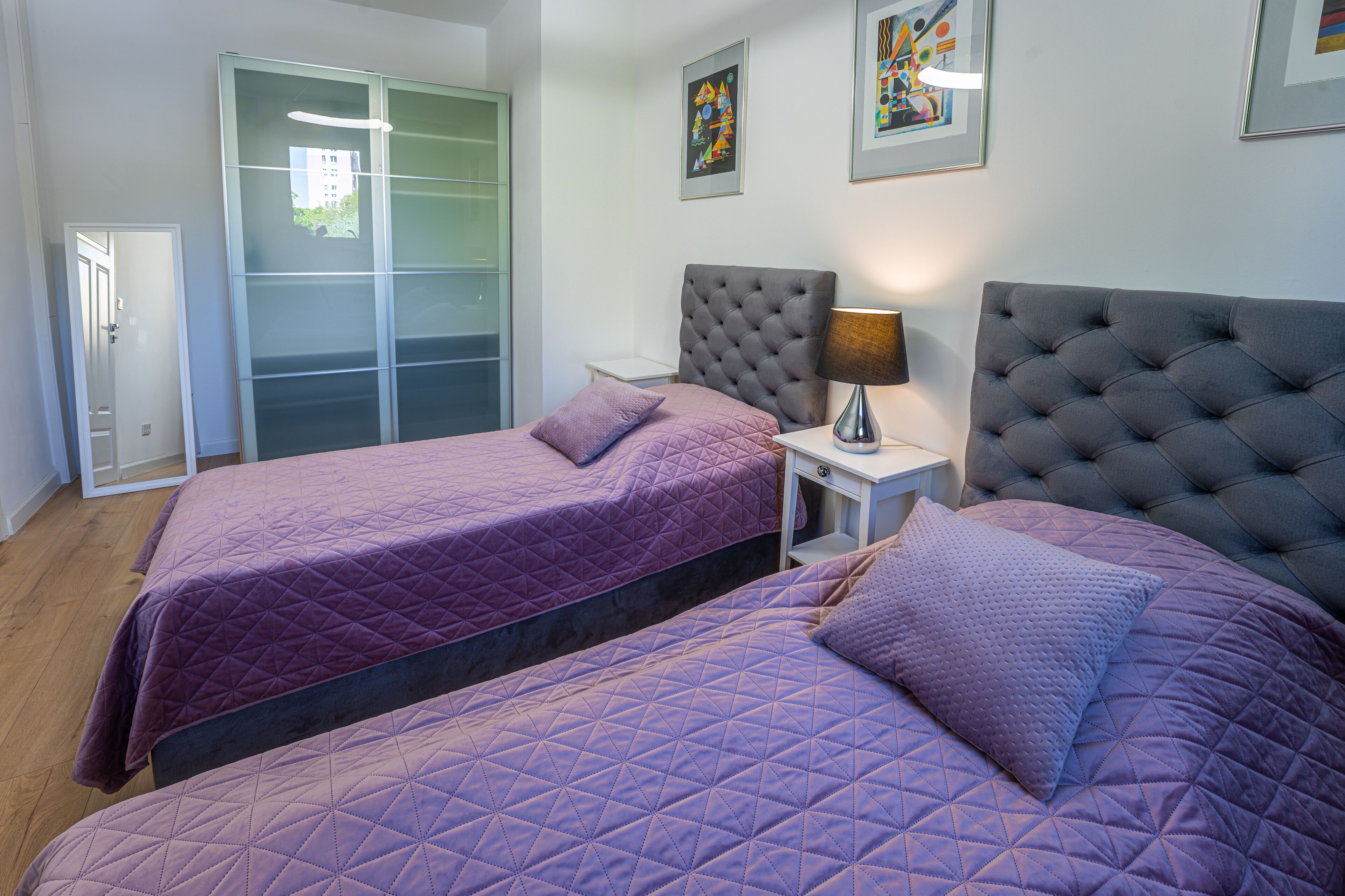A bedroom with two beds, a wardrobe, and artwork on the walls.