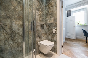 Un baño con ducha de vidrio, inodoro blanco y pared de mármol.