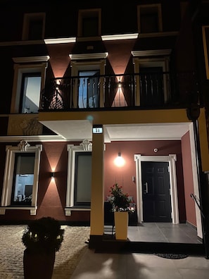 Un edificio de varios pisos con una entrada bien iluminada, ventanas amplias y un balcón con barandillas.