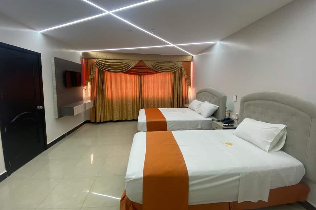 A hotel room with two beds, a TV mounted on the wall, and a curtain with a golden pattern.