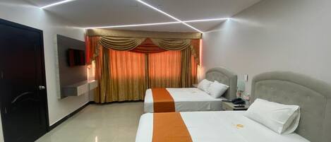 Habitación de hotel con dos camas, un televisor montado en la pared y una cortina con estampado dorado.