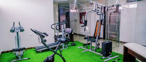 Un gimnasio con diversos equipos de ejercicio, incluyendo una caminadora, elíptica y máquinas de pesas, sobre un piso verde.