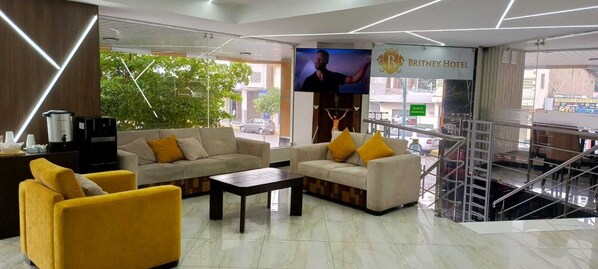 Vestíbulo de hotel con sofás, una cafetera y una pantalla de televisión.