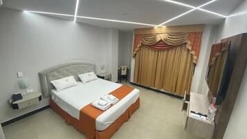 Una habitación de hotel con una cama grande, un escritorio, una silla, un televisor de pantalla plana y una cortina.