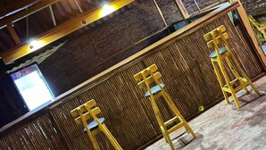 A covered outdoor seating area with wooden tables and chairs, a bamboo partition, and a television screen. - Ocean View (Riohacha)