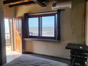 A room with a bed, a window with curtains, a small table, and an air conditioning unit. - Ocean View  (Riohacha)