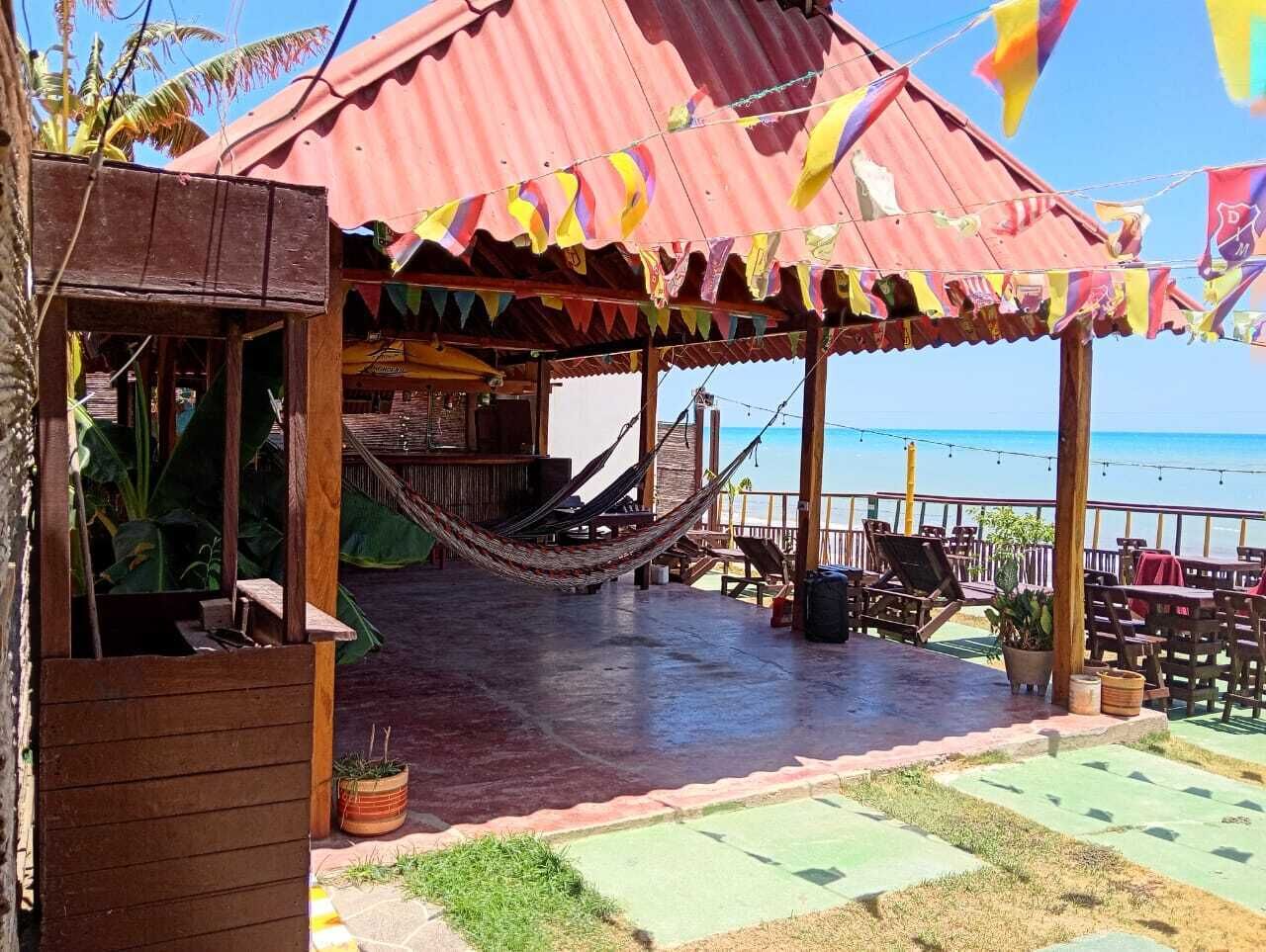 Ein überdachter Außenbereich mit Hängematte, Holzmöbeln und Blick auf den Strand.