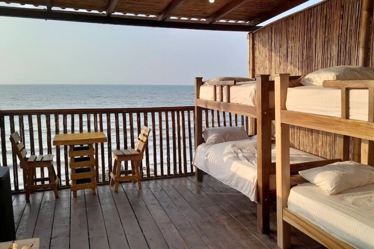 A wooden deck with bunk beds and a table, overlooking the sea.