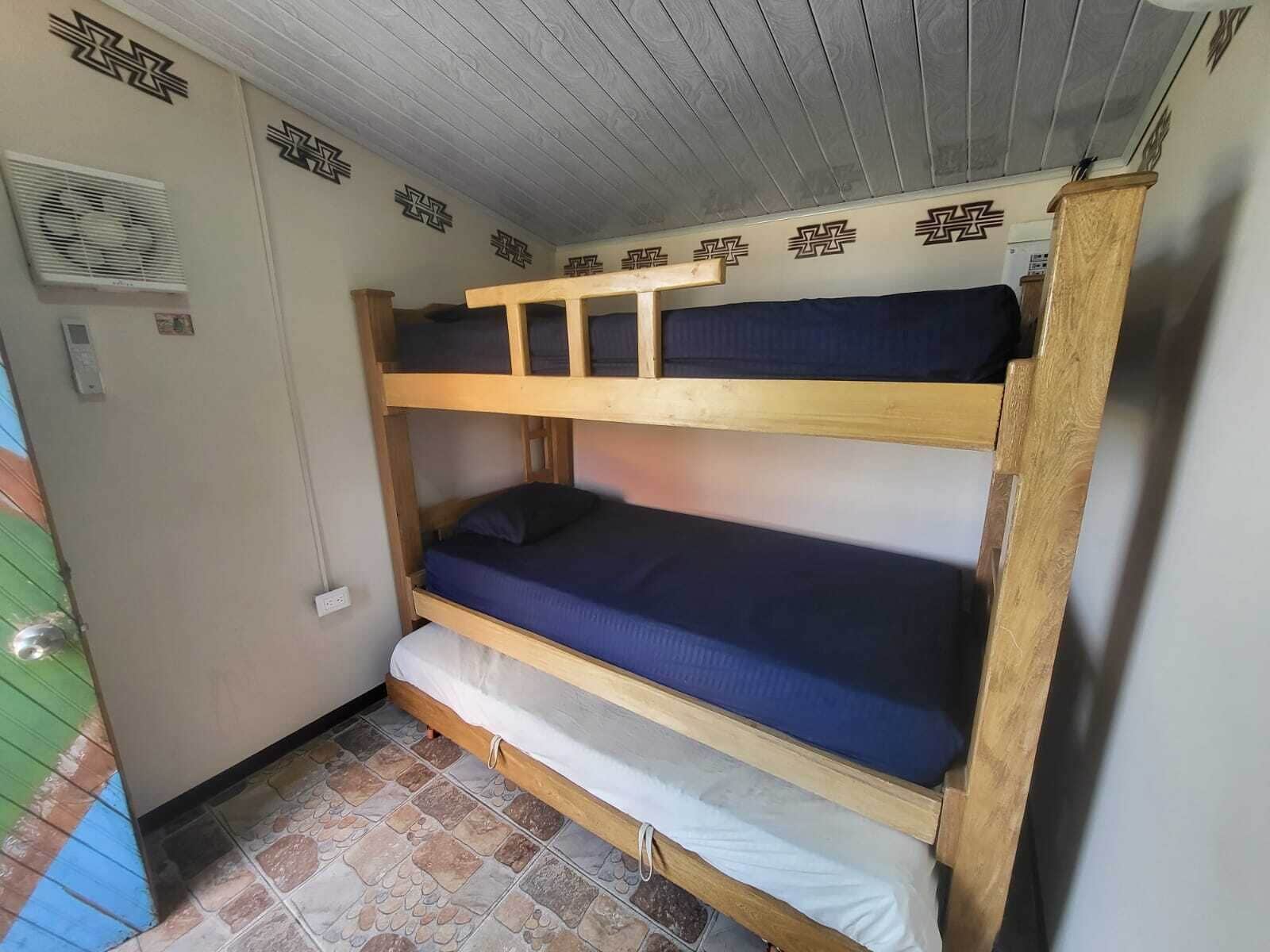 A bunk bed room with a wooden frame, a lower bunk with a white mattress, and a top bunk with a blue mattress.