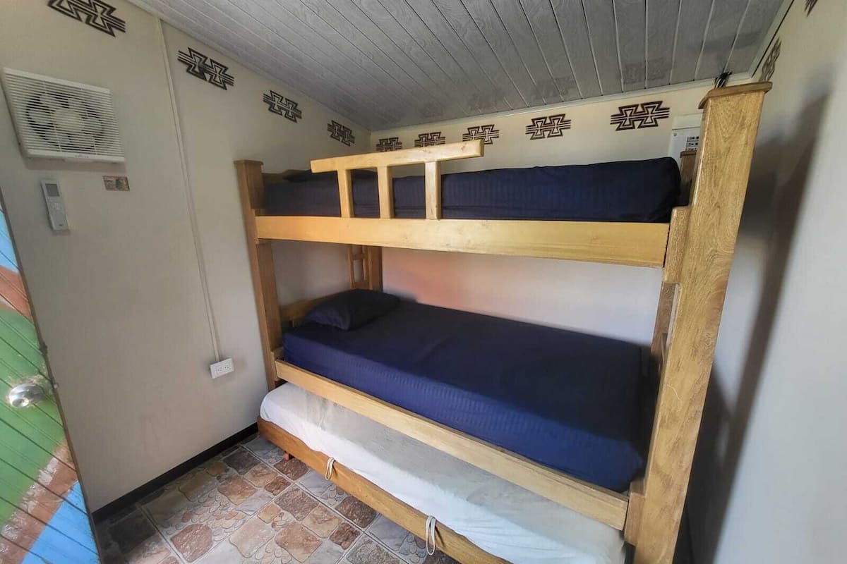 A bunk bed room with a wooden frame, a lower bunk with a white mattress, and a top bunk with a blue mattress.