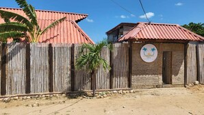 A rustic building with a corrugated metal roof, a wooden fence, and a sign with palm trees. - Ocean View (Riohacha)