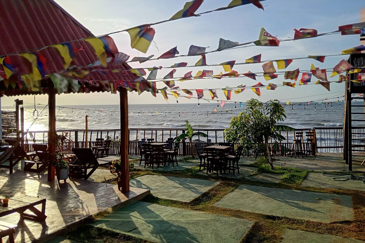 A coastal outdoor seating area with tables and chairs, a railing, and a view of the ocean.