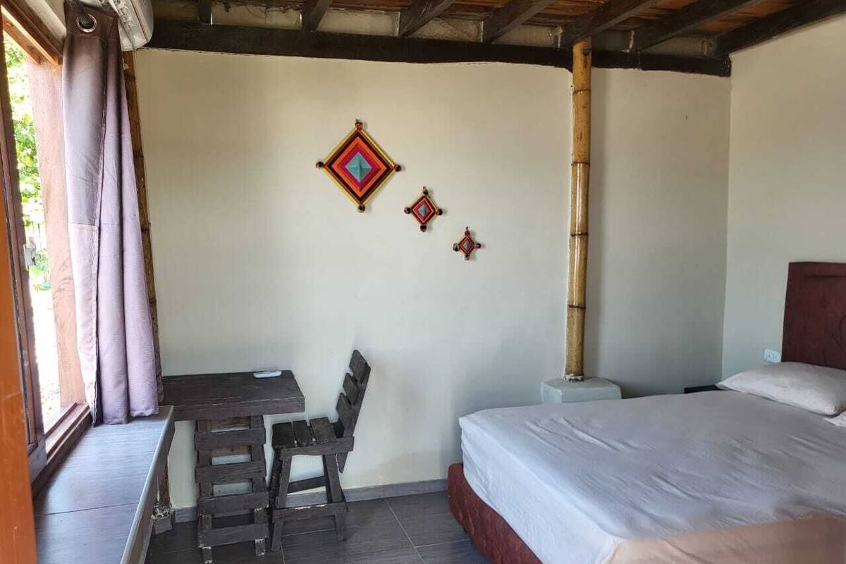 A room with a bed, a desk, and a chair. There are decorative wall hangings and a bamboo pillar.
