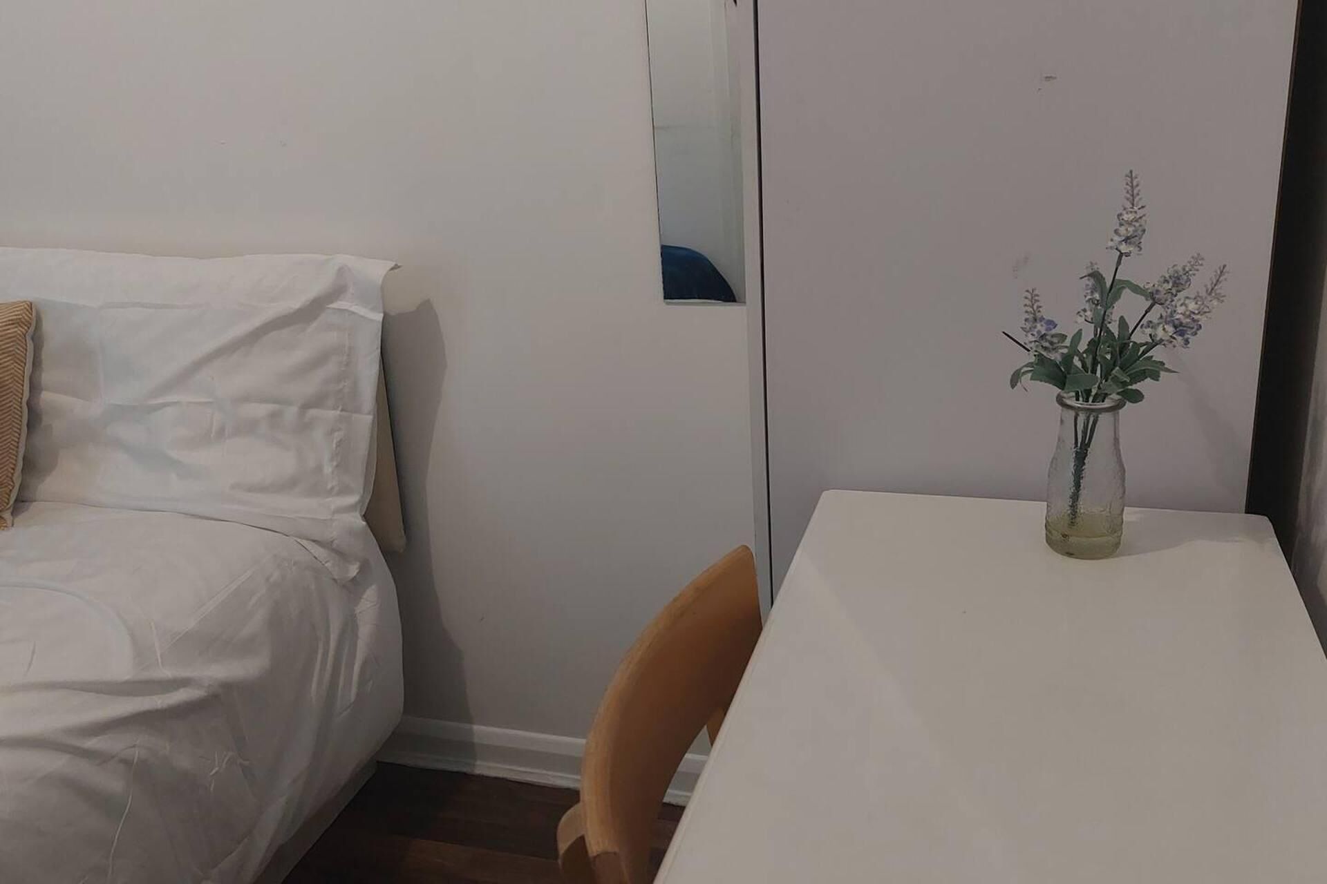 Ein Schlafzimmer mit einem Bett, einem kleinen Tisch mit Blumenvase und einem Stuhl.