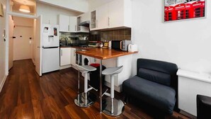 A compact kitchen with a wooden countertop, white cabinets, and a black chair. - Apartment Sleeps 7 With Wifi (London)