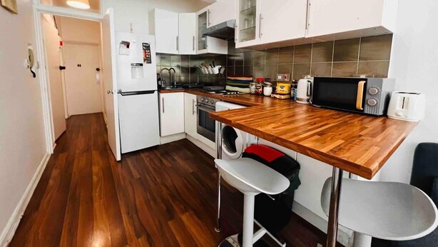 A compact kitchen with white cabinets, a wooden countertop, a microwave, a toaster, and a sink. - Apartment Sleeps 7 With Wifi (London)