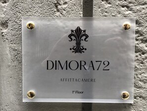 A sign with the text "DIMORA72 AFFITTACAMERE 1st Floor" mounted on a textured wall.