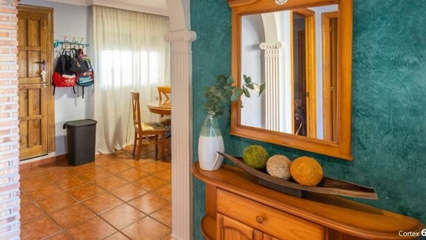 Um quarto com parede de tijolos, um armário de madeira com espelho e um vaso verde sobre uma prateleira de madeira.