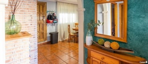 Una habitación con pared de ladrillo, un armario de madera con espejo y un florero verde sobre un estante de madera.