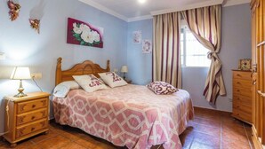 Quarto com cama, mesa de cabeceira, penteadeira e janela com cortinas.