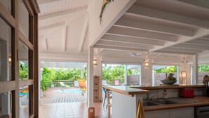 Cozinha moderna com uma ilha grande, área de refeições com assentos externos e vista para uma piscina e vegetação.