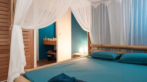 Quarto com cama, mesa de cabeceira, abajur e banheiro visível por uma porta aberta.