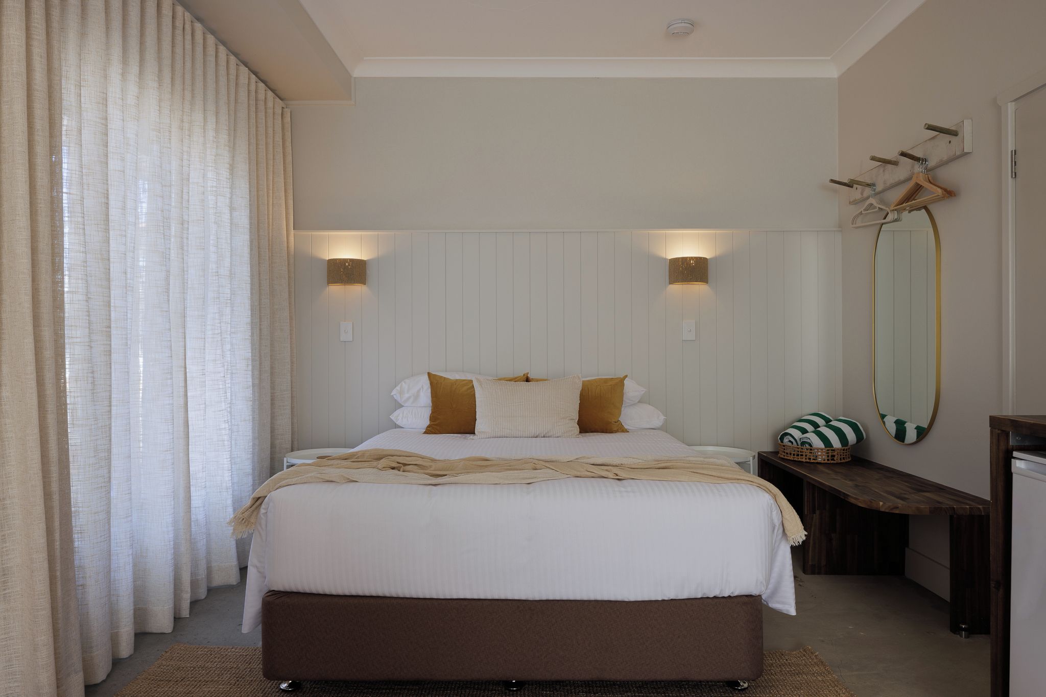 A bedroom with a bed, bedside tables, a mirror, and a wall-mounted light fixture.