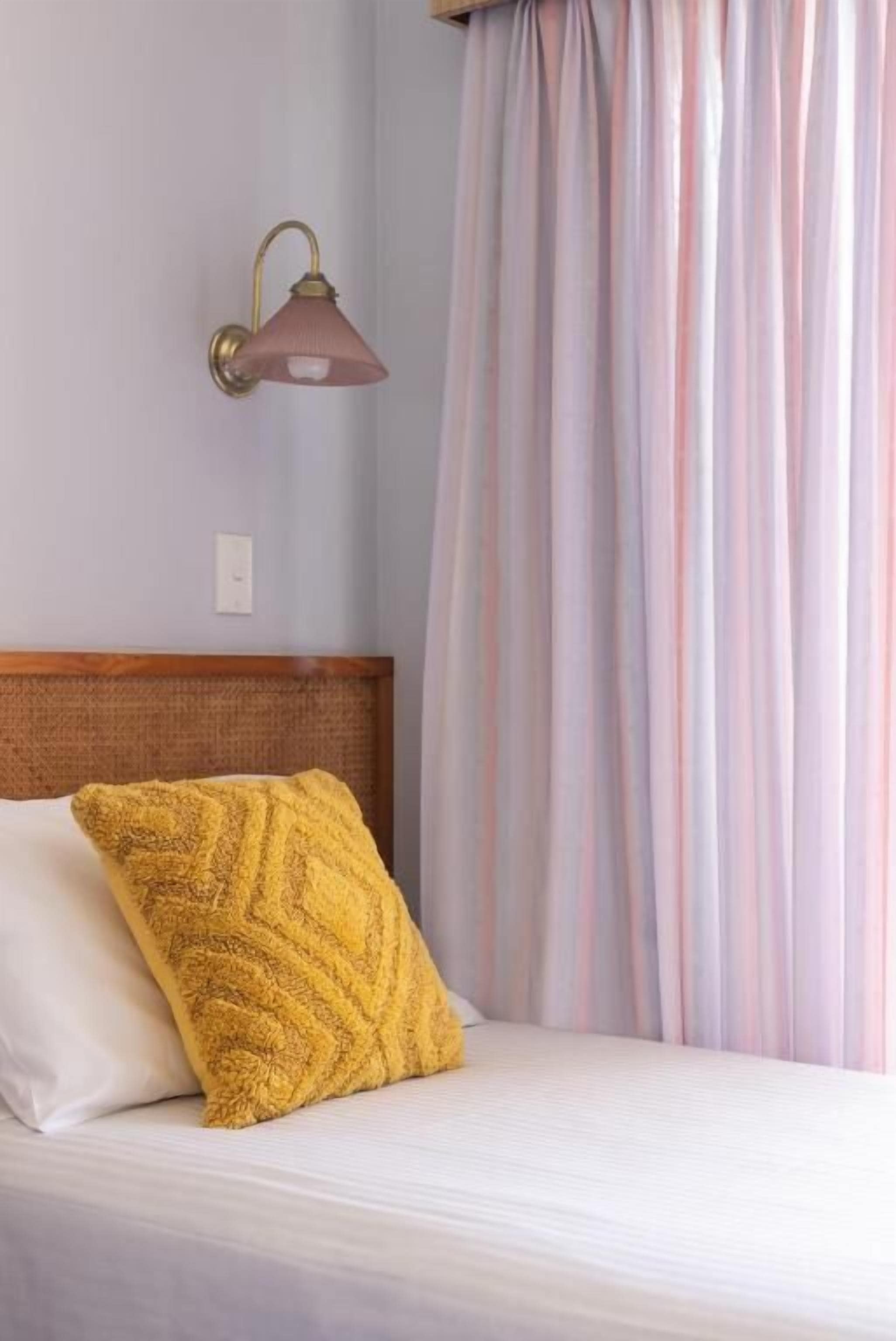 Ein Bett mit Holz-Kopfteil, einem gelb gemusterten Kissen und einer Wandlampe.