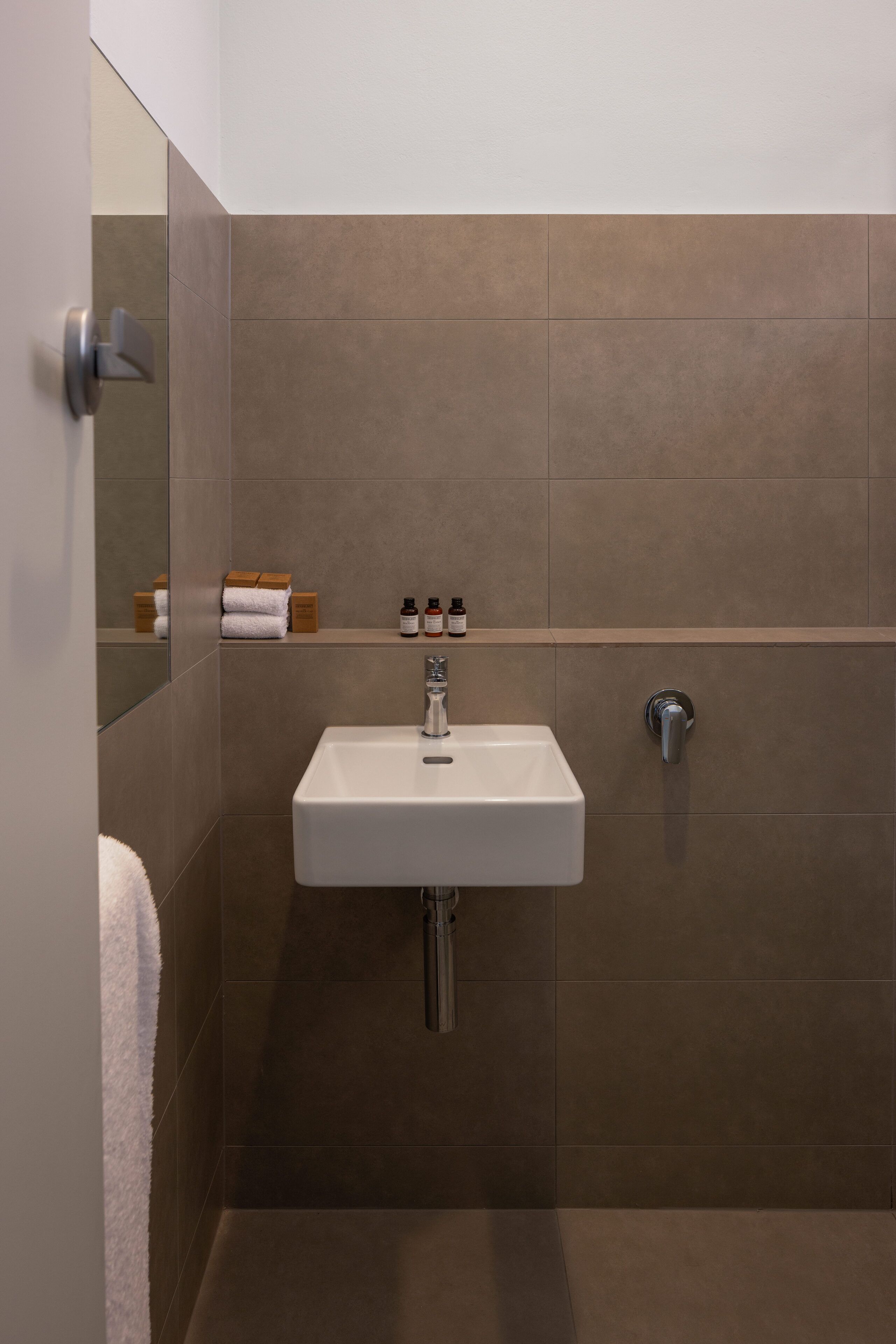 Un baño con lavamanos blanco, un espejo y un perchero para toallas.