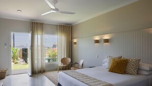 A hotel room with a large bed, a ceiling fan, a small table with chairs, and a view of the outdoors.