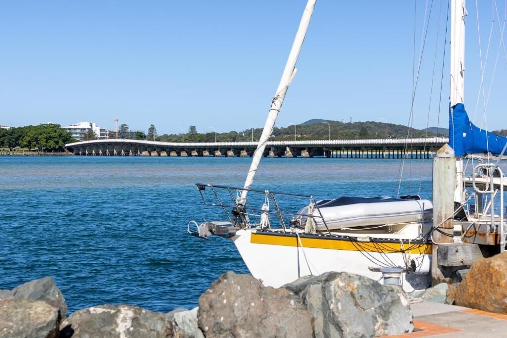 Un velero amarrado cerca de un muelle, con un puente al fondo.