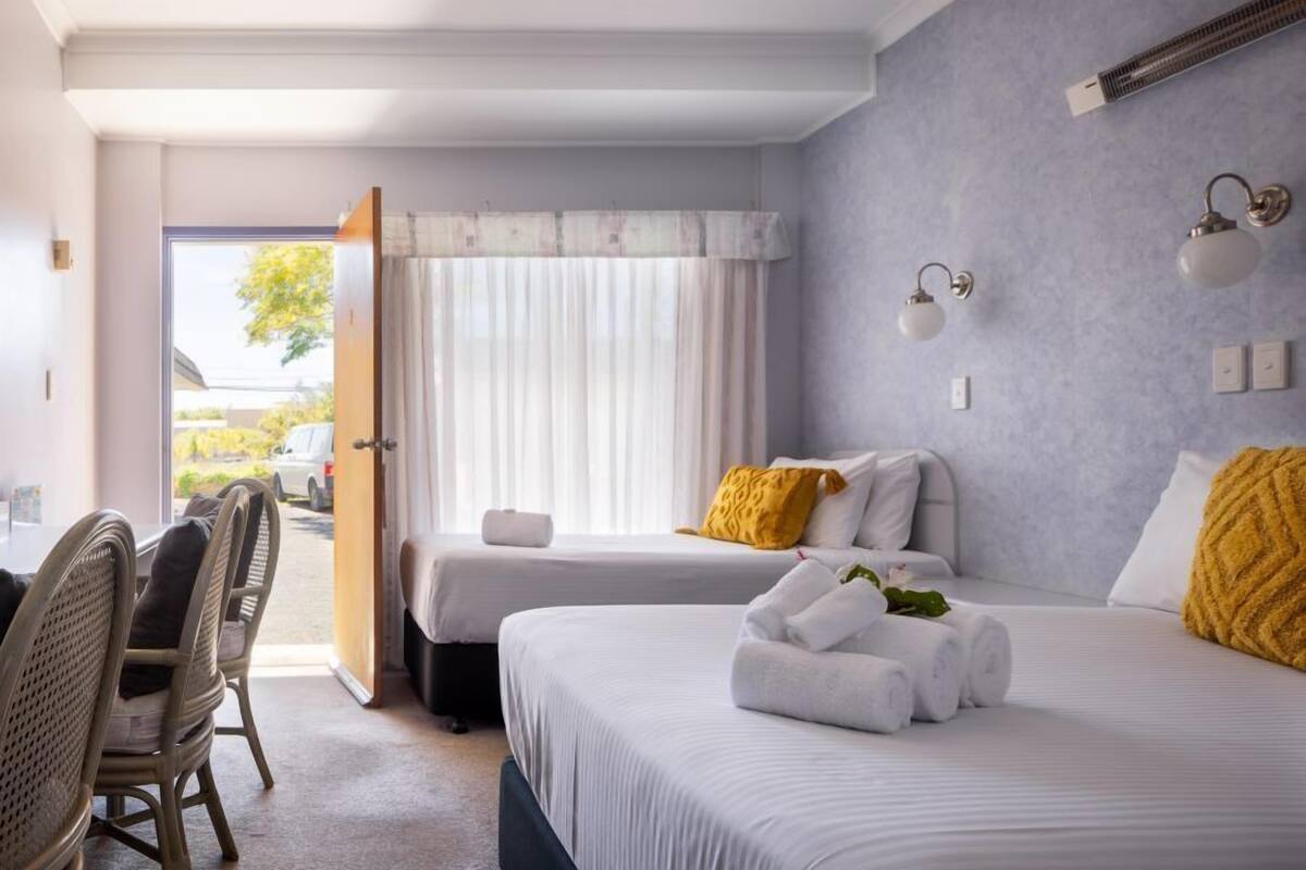Habitación de hotel con dos camas, una zona de comedor con sillas de mimbre y vistas al exterior.