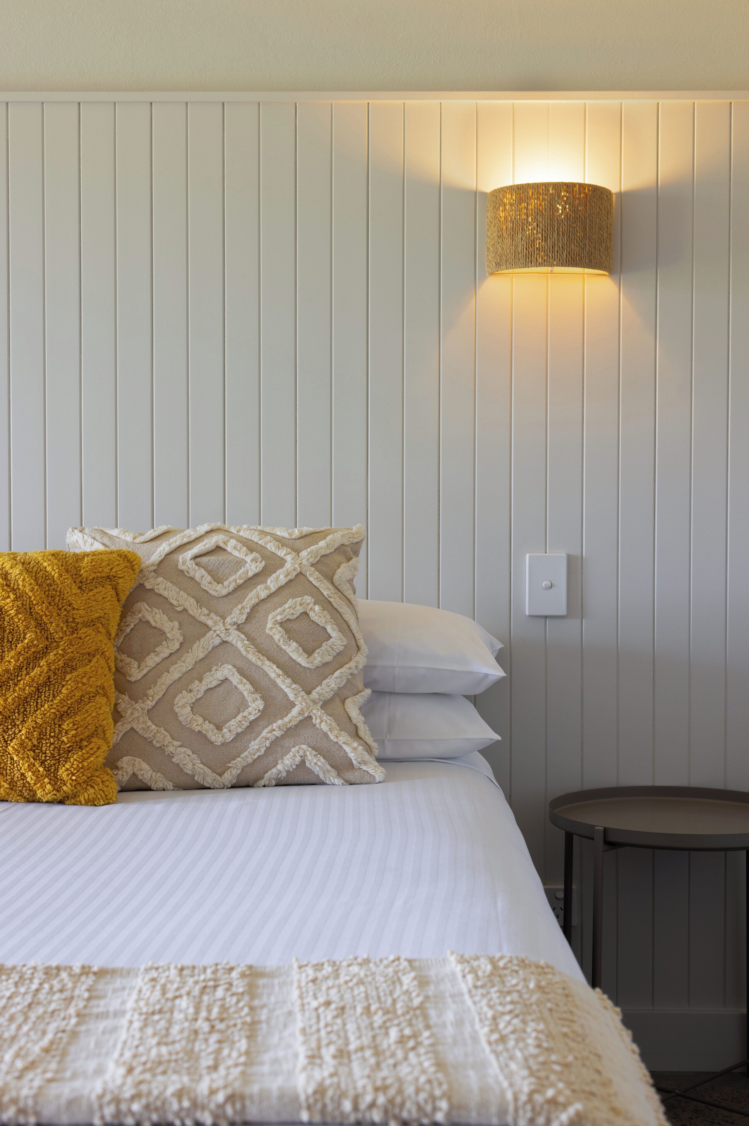 A neatly made bed with patterned pillows, a bedside lamp, and a small round table.