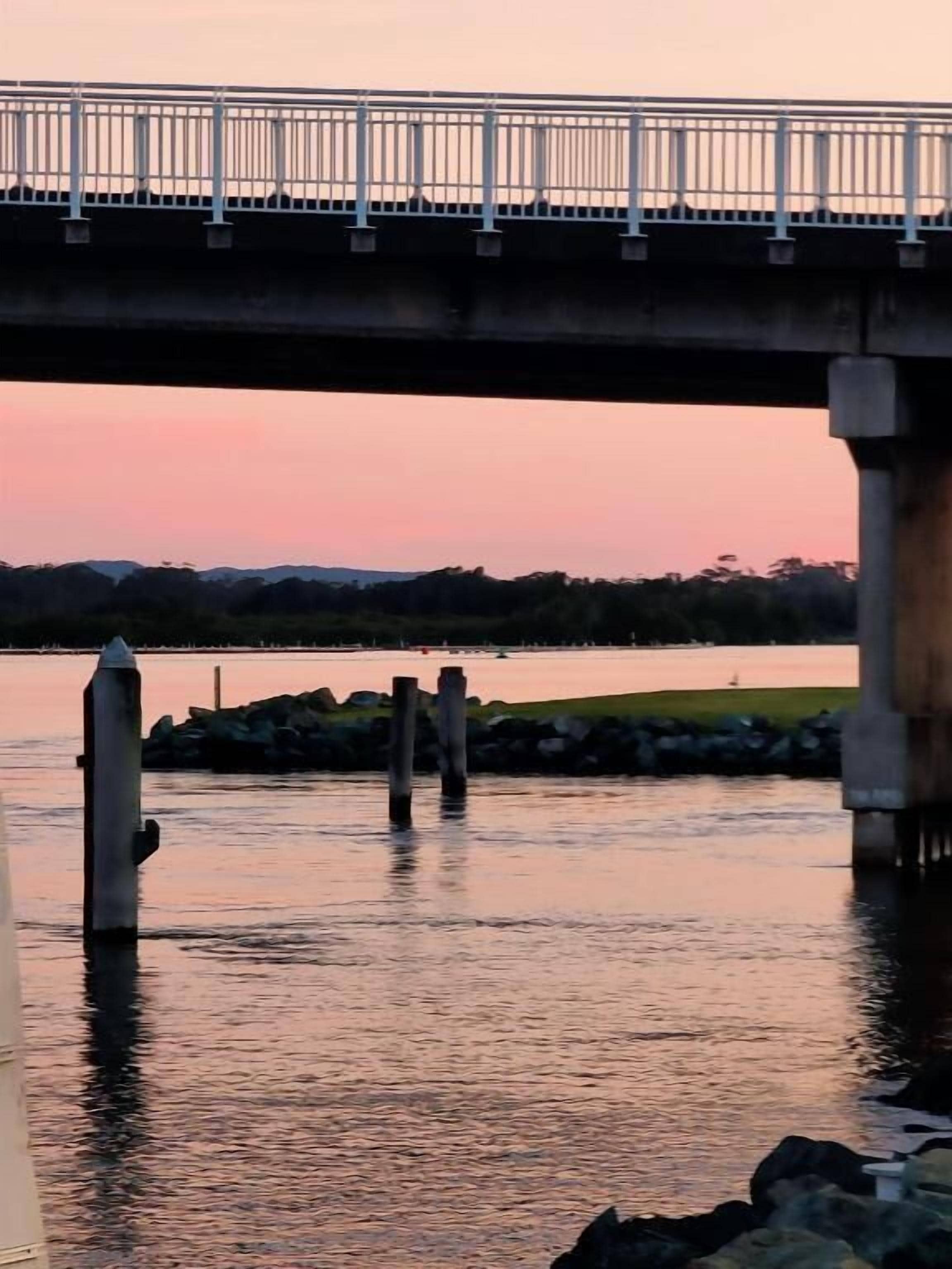 A bridge over calm water with a sunset in the background.