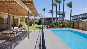 A pool area with picnic tables, a covered seating area, and palm trees.