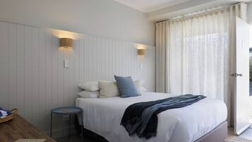 Quarto com cama, abajures, uma mesinha e vista através de uma porta.