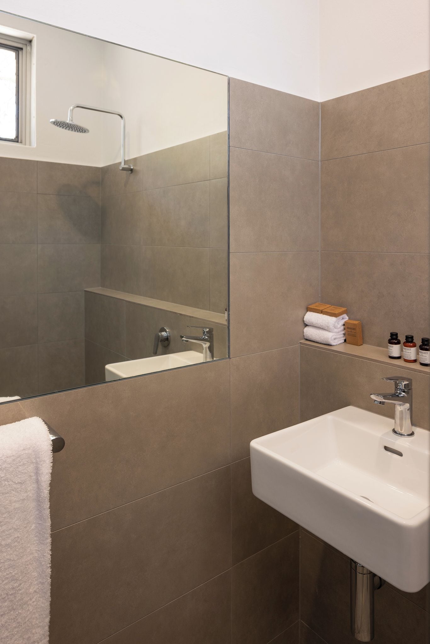 A modern bathroom with a large mirror, a white sink, and a shower.