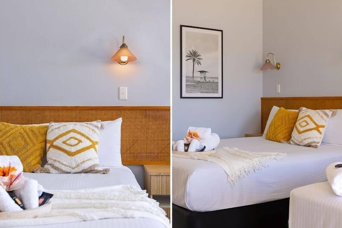 Una habitación de hotel con una cama, una mesita de noche, una lámpara de pared y un cuadro enmarcado.