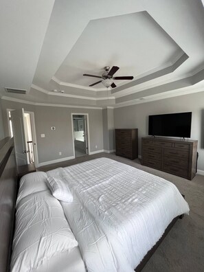 A bedroom with a large bed, a ceiling fan, a dresser, and a TV.