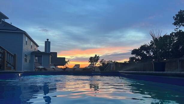 Una piscina con sillas de descanso y una casa al fondo durante el atardecer.