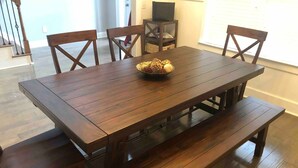 Una mesa de madera con bancos, una cesta de pan y un mueble de televisión al fondo.