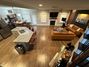A modern kitchen with a granite countertop, a dining area with orange chairs, a living room with a brown leather sofa, and a fireplace.