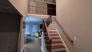 Un hall espacioso con una escalera de madera que sube a un segundo piso, una araña y un comedor con mesa y sillas.