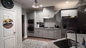 Cocina moderna con encimeras de granito, electrodomésticos de acero inoxidable e iluminación colgante.