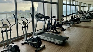 Une salle de sport équipée de divers appareils de cardio, dotée de grandes fenêtres et offrant une vue sur un pont.