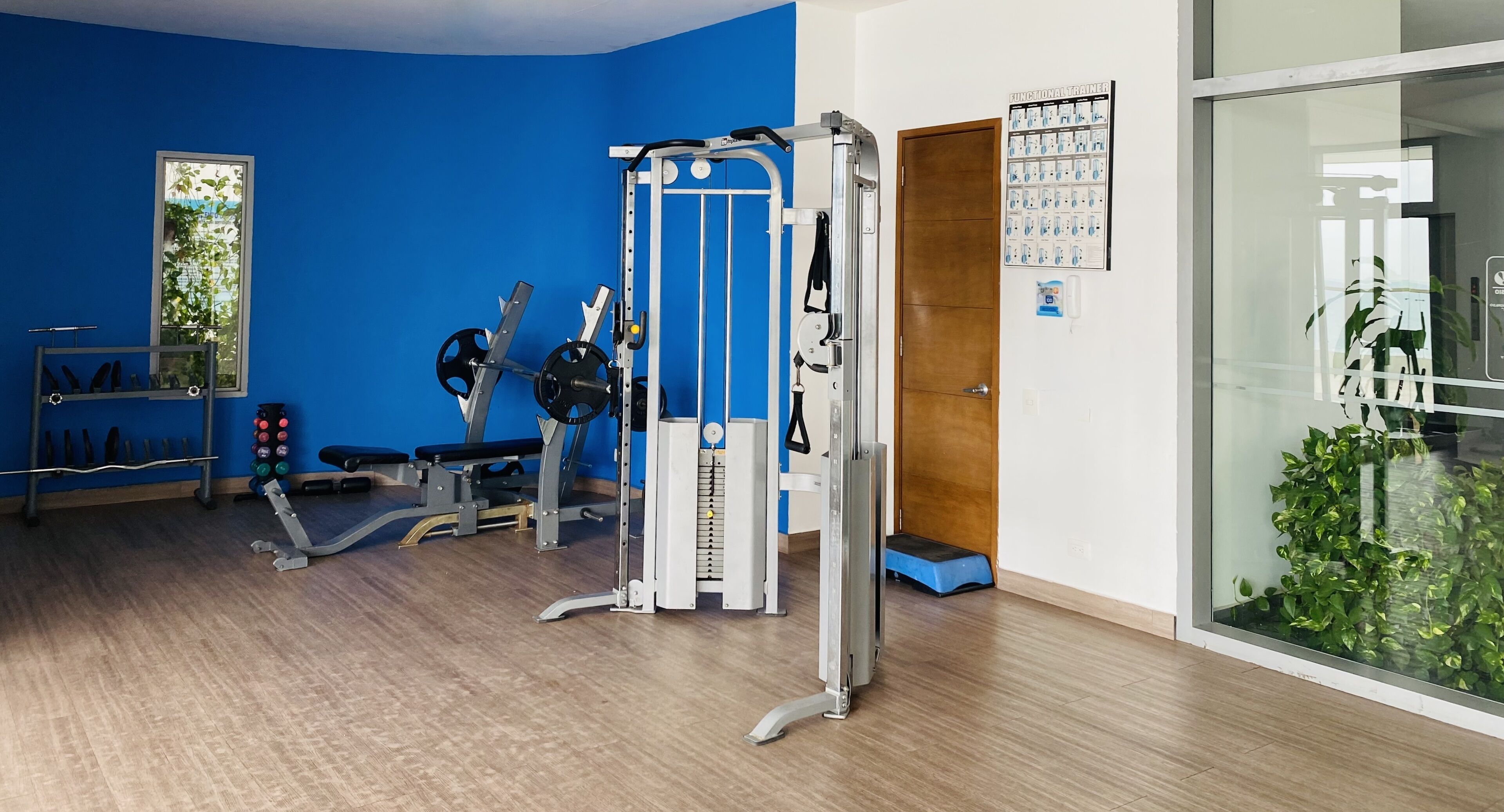Ein Fitnessraum mit Trainingsgeräten, einem Spiegel und einer Tür zu einem weiteren Raum.