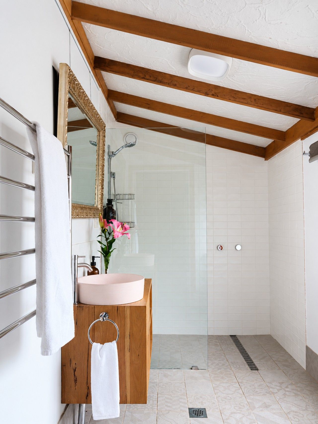A bathroom with a wooden vanity, a round sink, a mirror, a shower, and a towel rack.