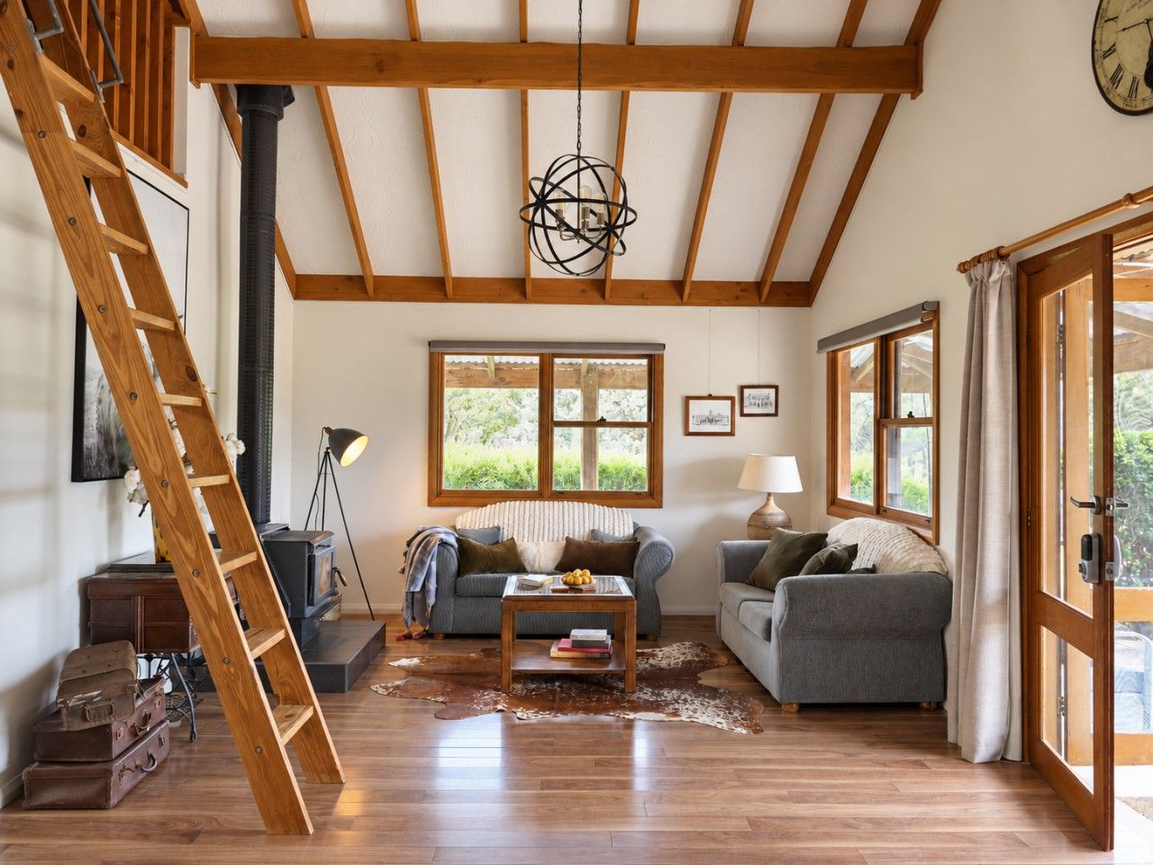 A spacious living room with wooden beams, a fireplace, a sofa, a coffee table, and a ladder.